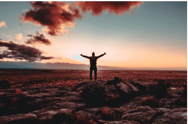 A person standing on a rocky plain with arms outstretched at sunset