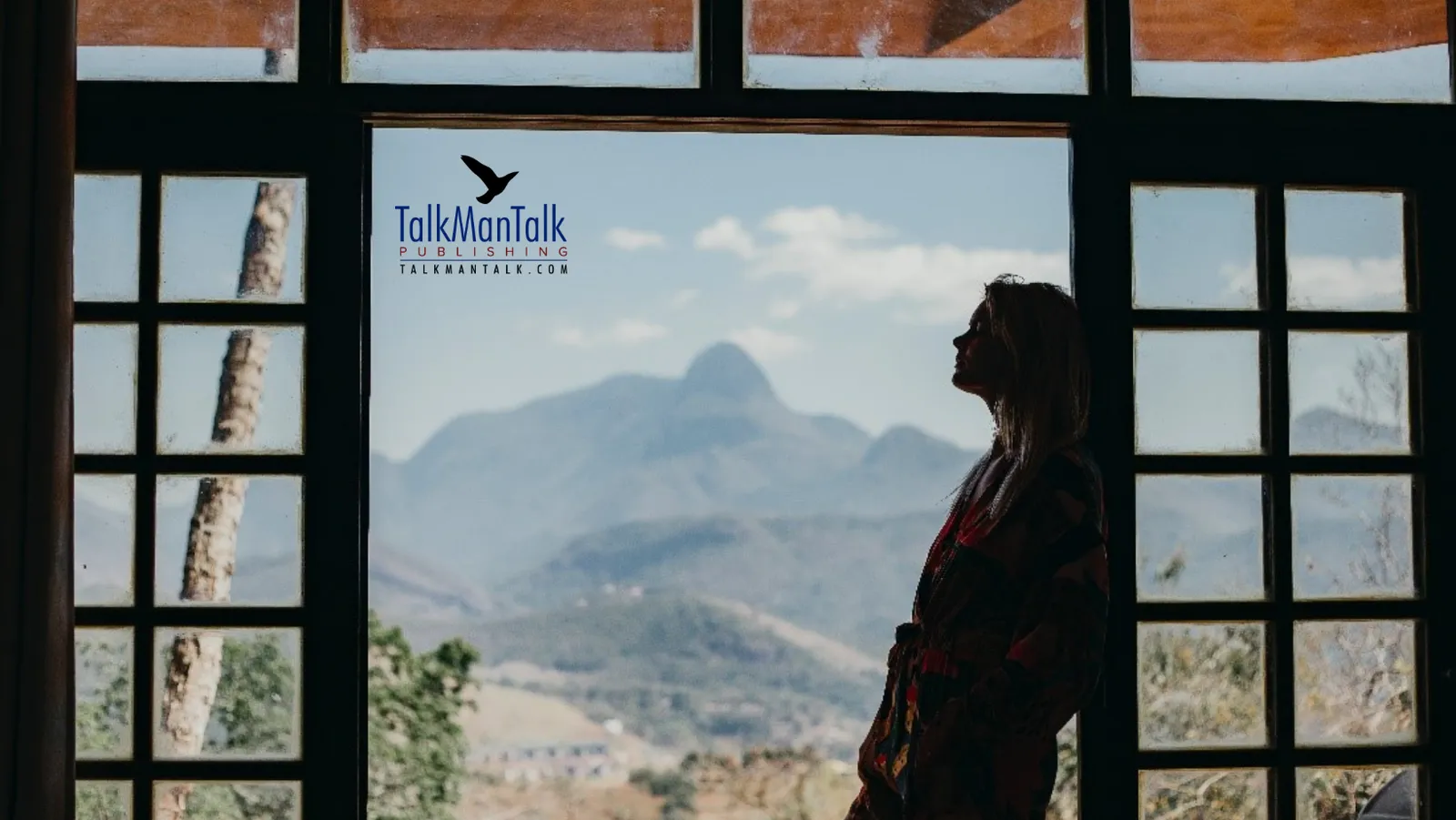 Silhouette of a woman looking out a window toward the mountains
