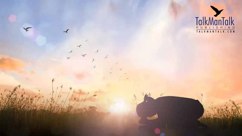 A person kneeling in prayer in a field at sunrise