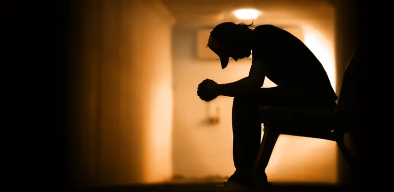 Silhouette of a person sitting with head bowed in a dimly lit room